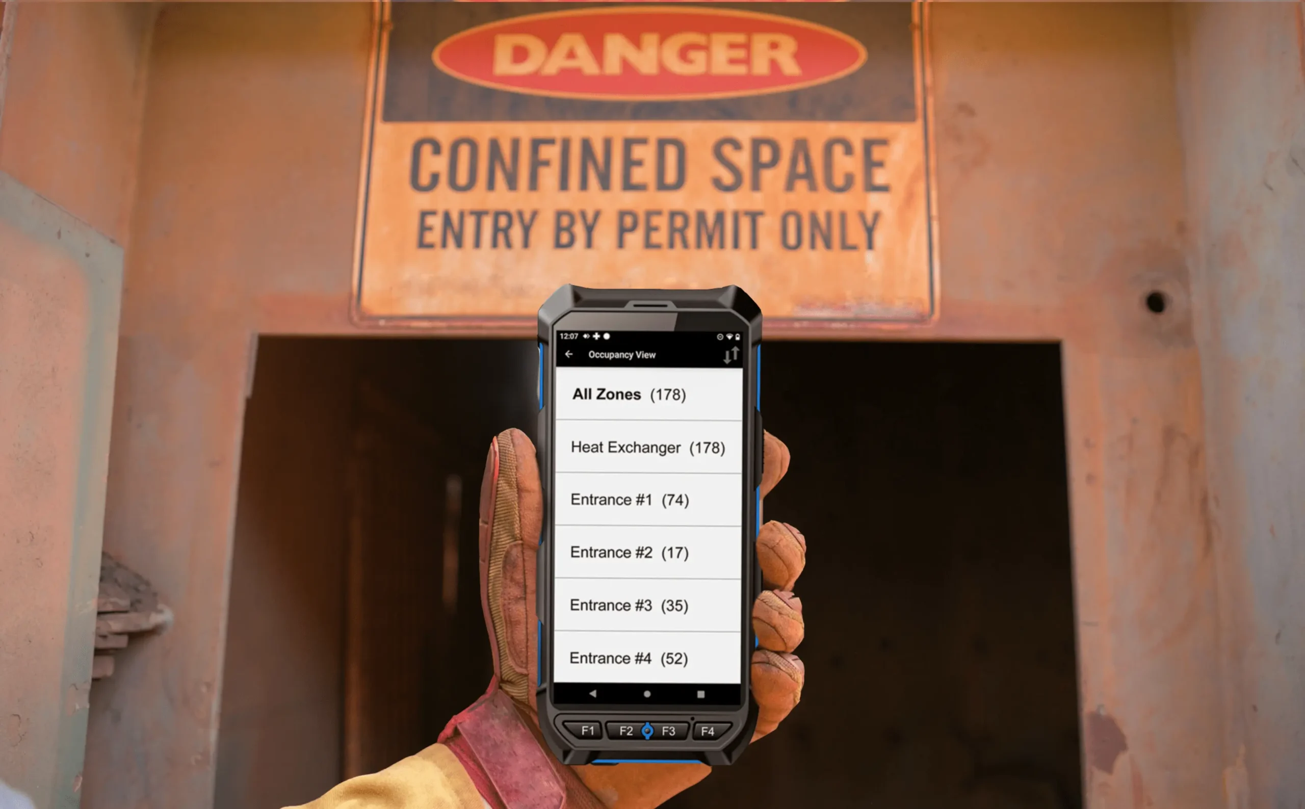 handheld device showing occupancy for different zone entrances in a gloved hand in front of a confined space opening and danger entry by permit only sign