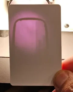 white security card being held up to a flashlight revealing the inner coil inside.