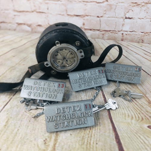 a mechanical clock on a leather strap on a table next to keys attached to metal tags